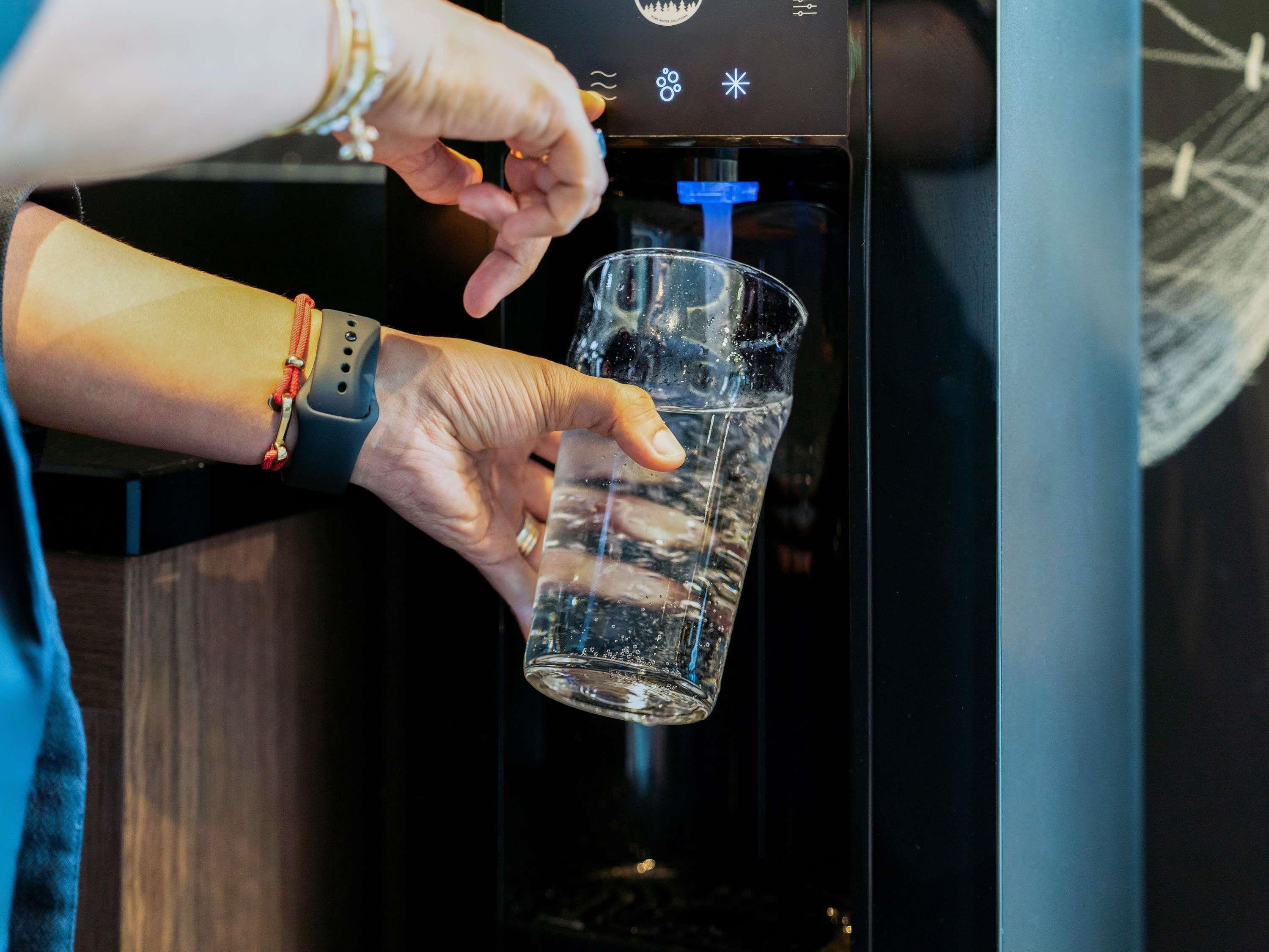 Une personne remplit un verre d’eau à l’aide d’un distributeur.