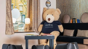 A room with a large teddy bear, a sofa, a table, and elephant-shaped stools. - Novotel Suites Paris Expo Porte de Versailles (Paris)