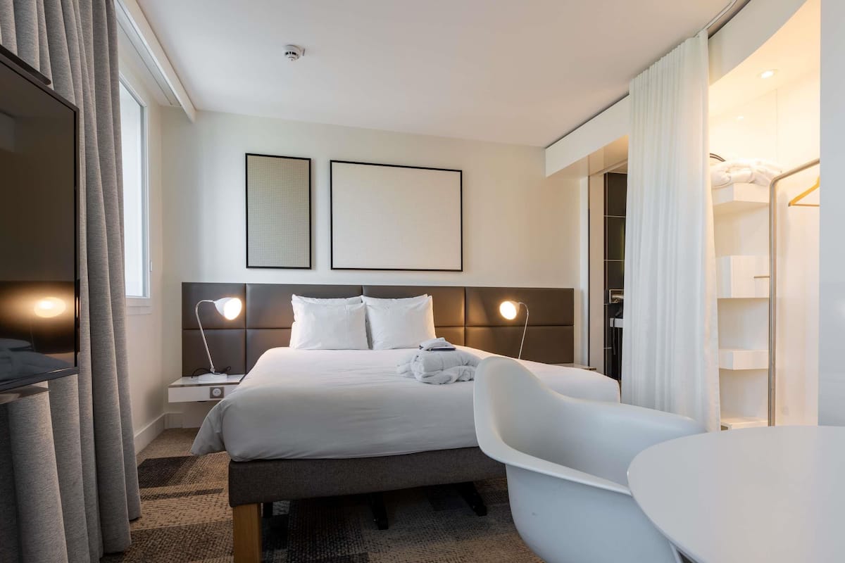 A hotel room with a bed, bedside tables, a desk, a chair, and a TV.