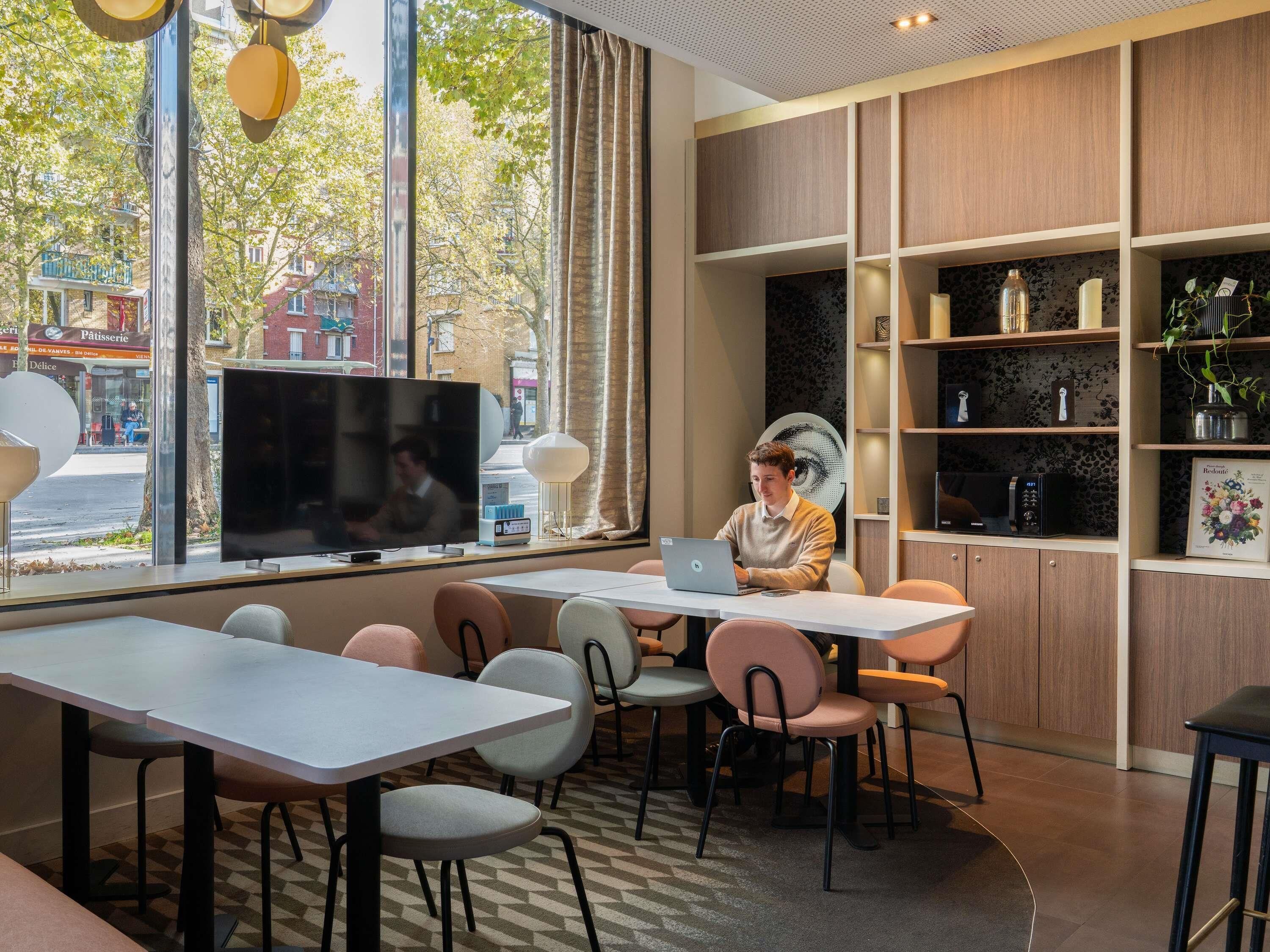 Un café moderne avec une grande fenêtre, un téléviseur à écran plat et un ordinateur portable posé sur une table.