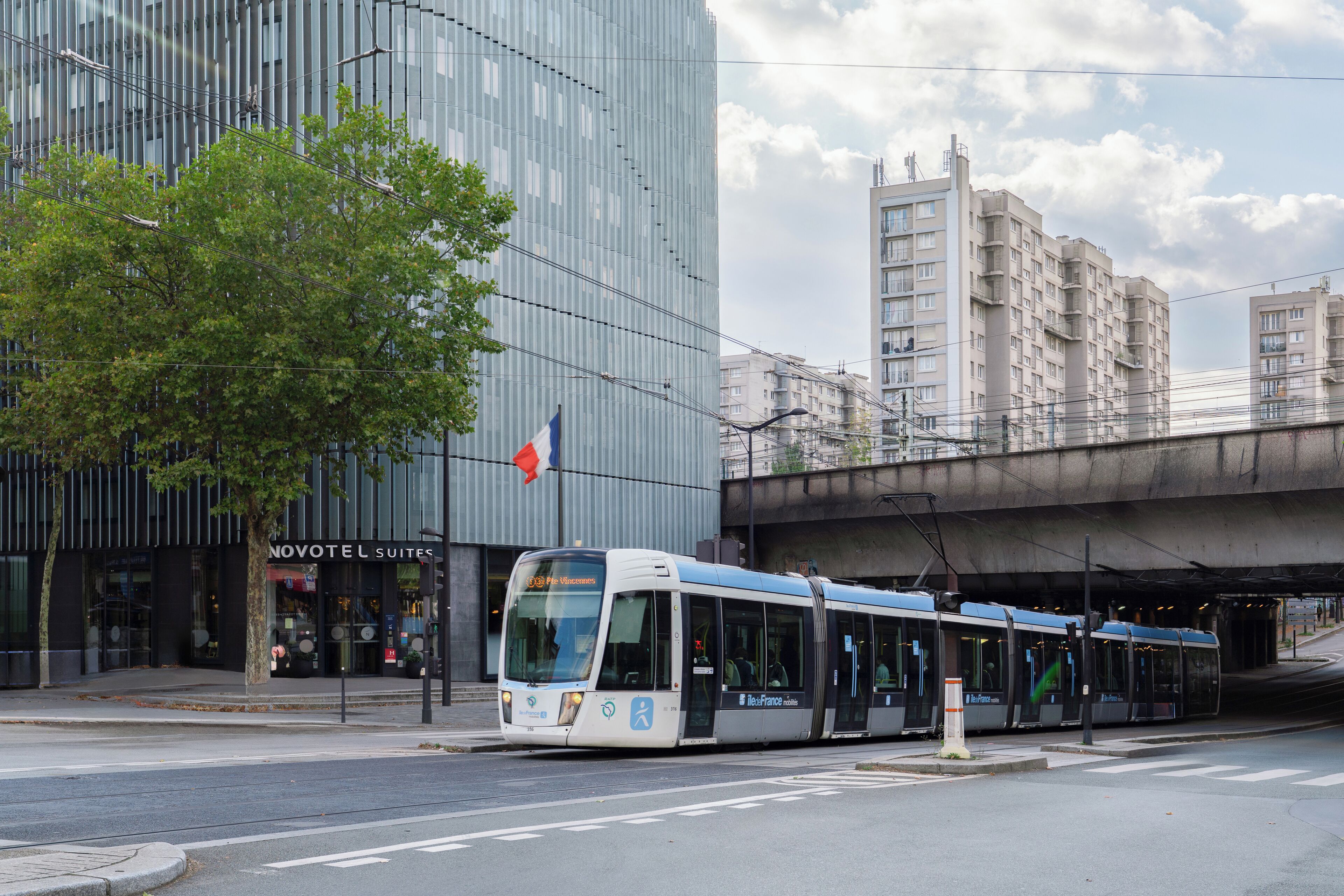 Un bâtiment moderne, avec une enseigne Novotel Suites, un tramway et un drapeau.