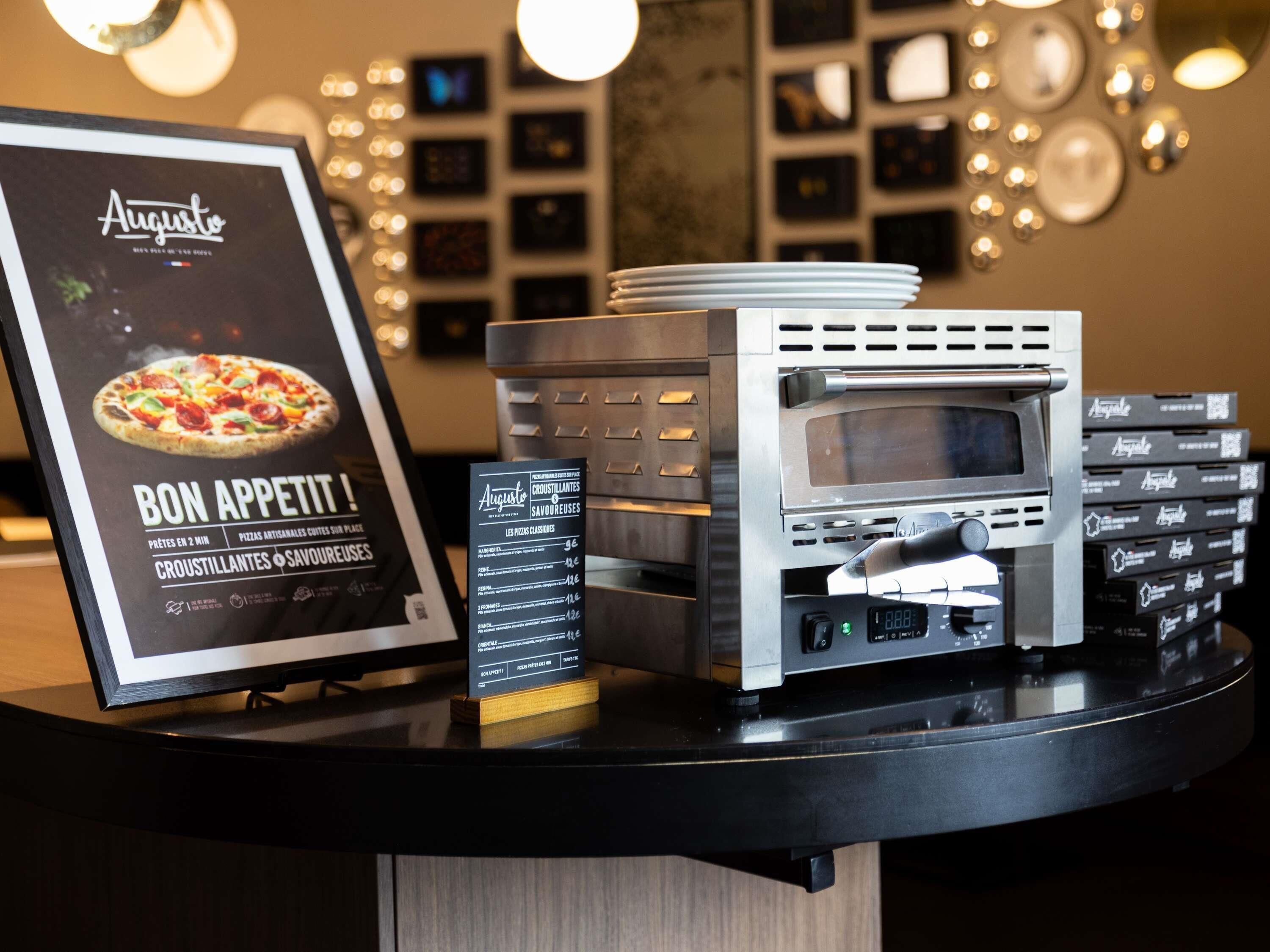 A pizza oven, a menu board, and a stack of pizza boxes on a counter.