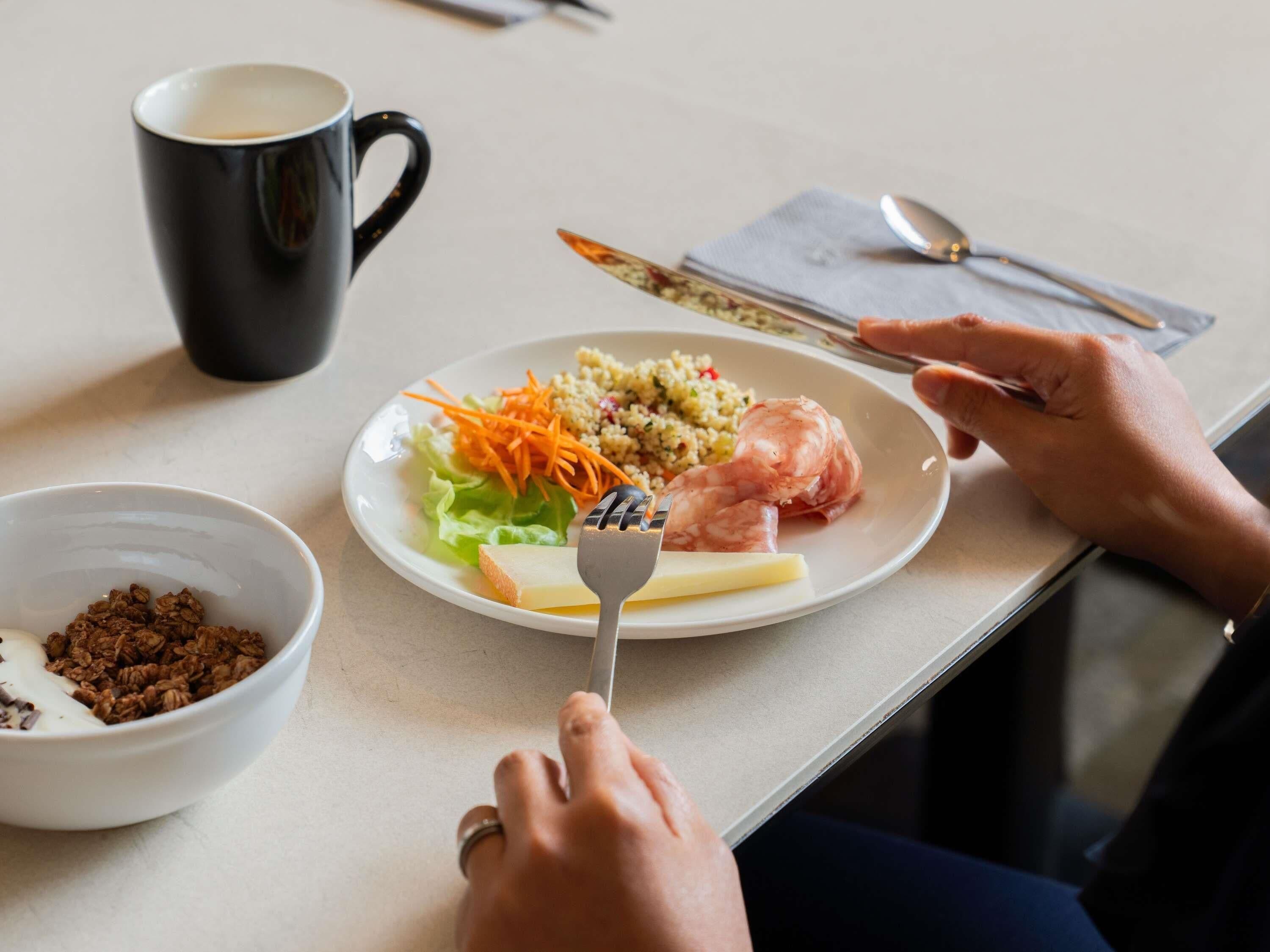 Une table à manger avec une assiette de nourriture, un bol de granola et une tasse de café.