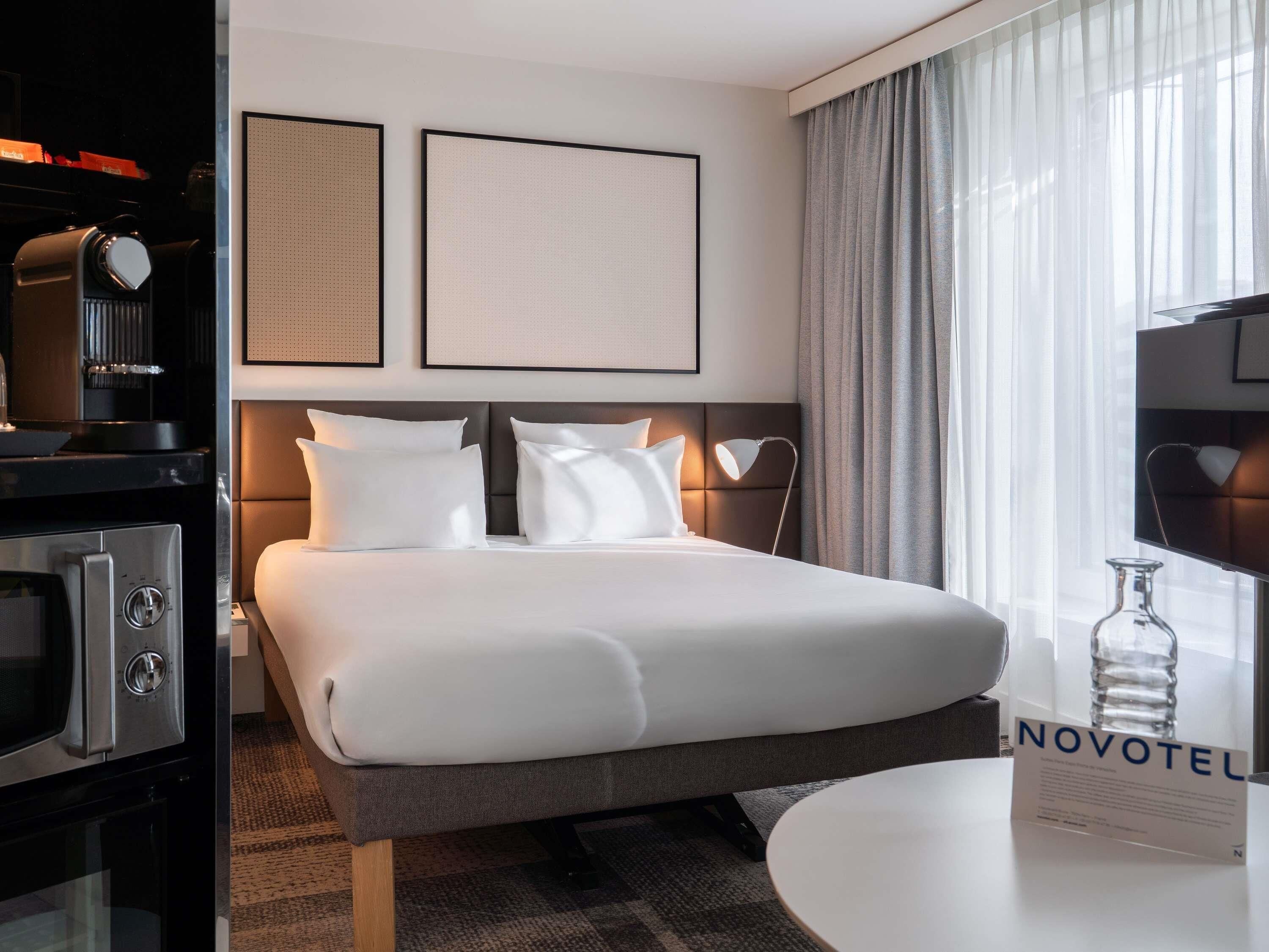 A hotel room with a bed, a desk, a TV, and a minibar.