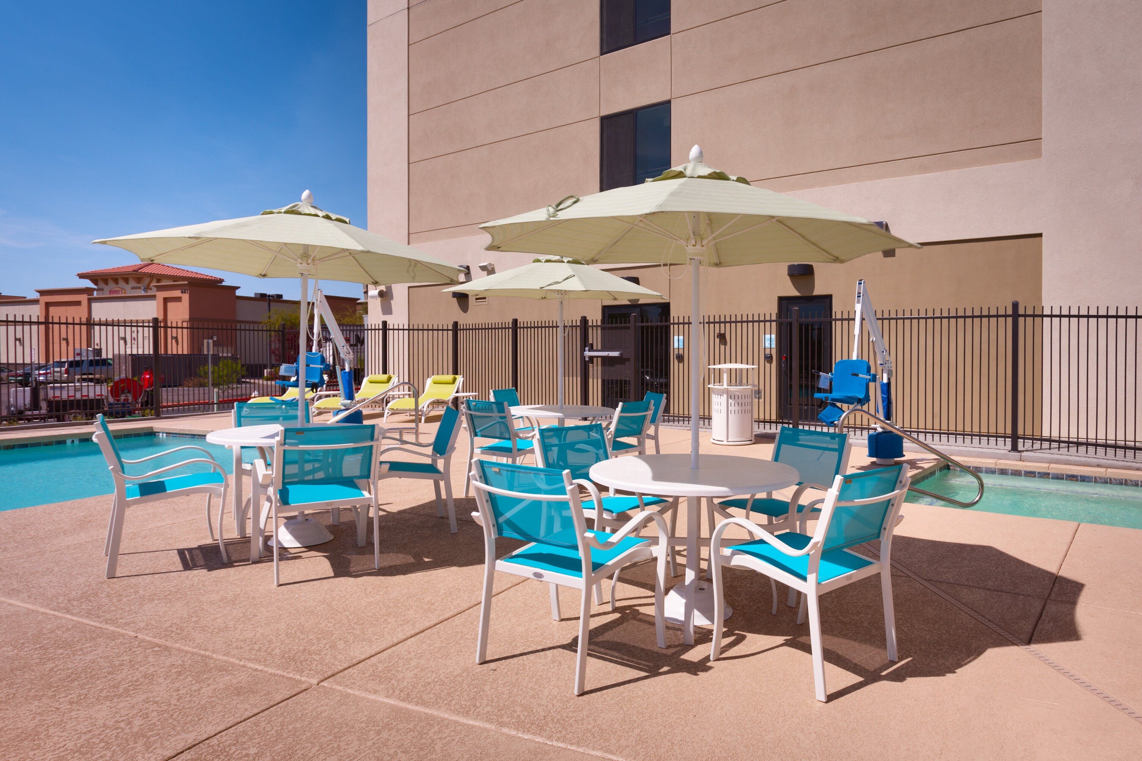 An outdoor pool area with lounge chairs and umbrellas, surrounded by a fence.