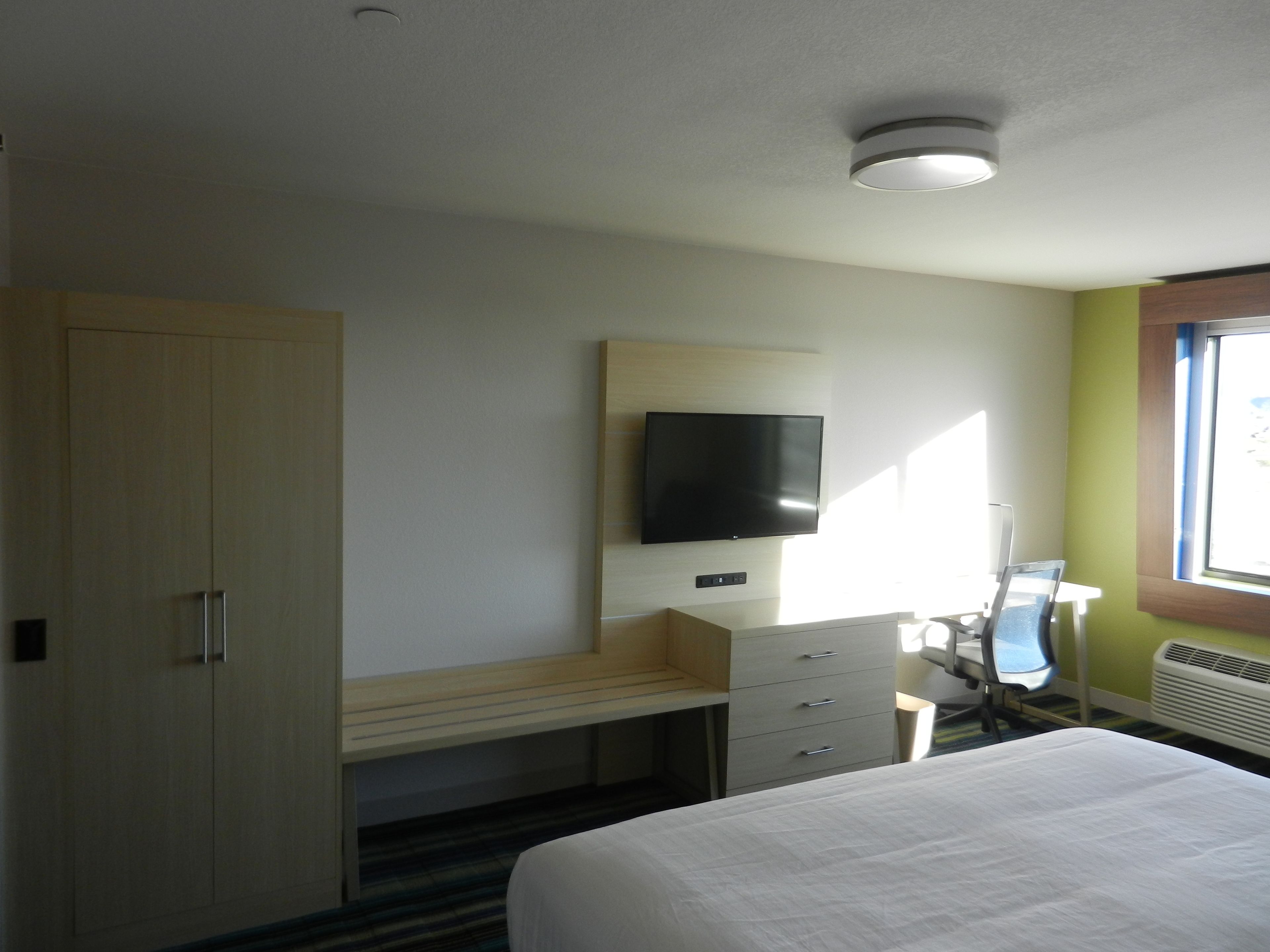 Ein Hotelzimmer mit Bett, Schreibtisch mit Stuhl, Wandfernseher und Kleiderschrank.