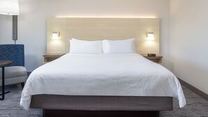 Une chambre d’hôtel avec un grand lit, deux tables de chevet avec des lampes, une petite table ronde et une chaise bleue.