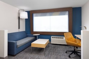 A modern room with a blue sofa, a wooden coffee table, a yellow office chair, a small round table, and a large window.