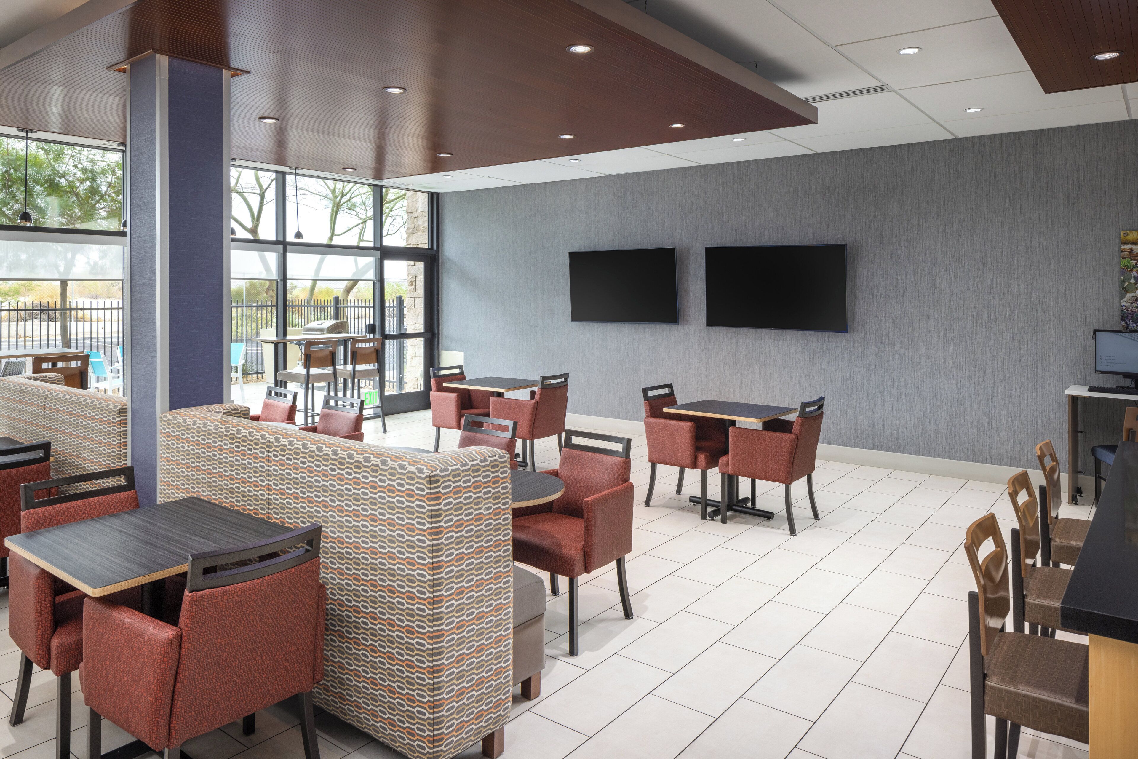 A modern indoor dining area with booths and tables, large windows, and flat-screen TVs on the wall.