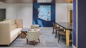 Un hall d’entrée moderne comprenant un canapé, des fauteuils, une table à manger et une grande fresque murale abstraite.