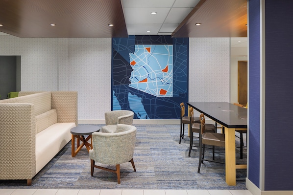A modern lobby with a sofa, chairs, a dining table, and a large abstract wall mural.