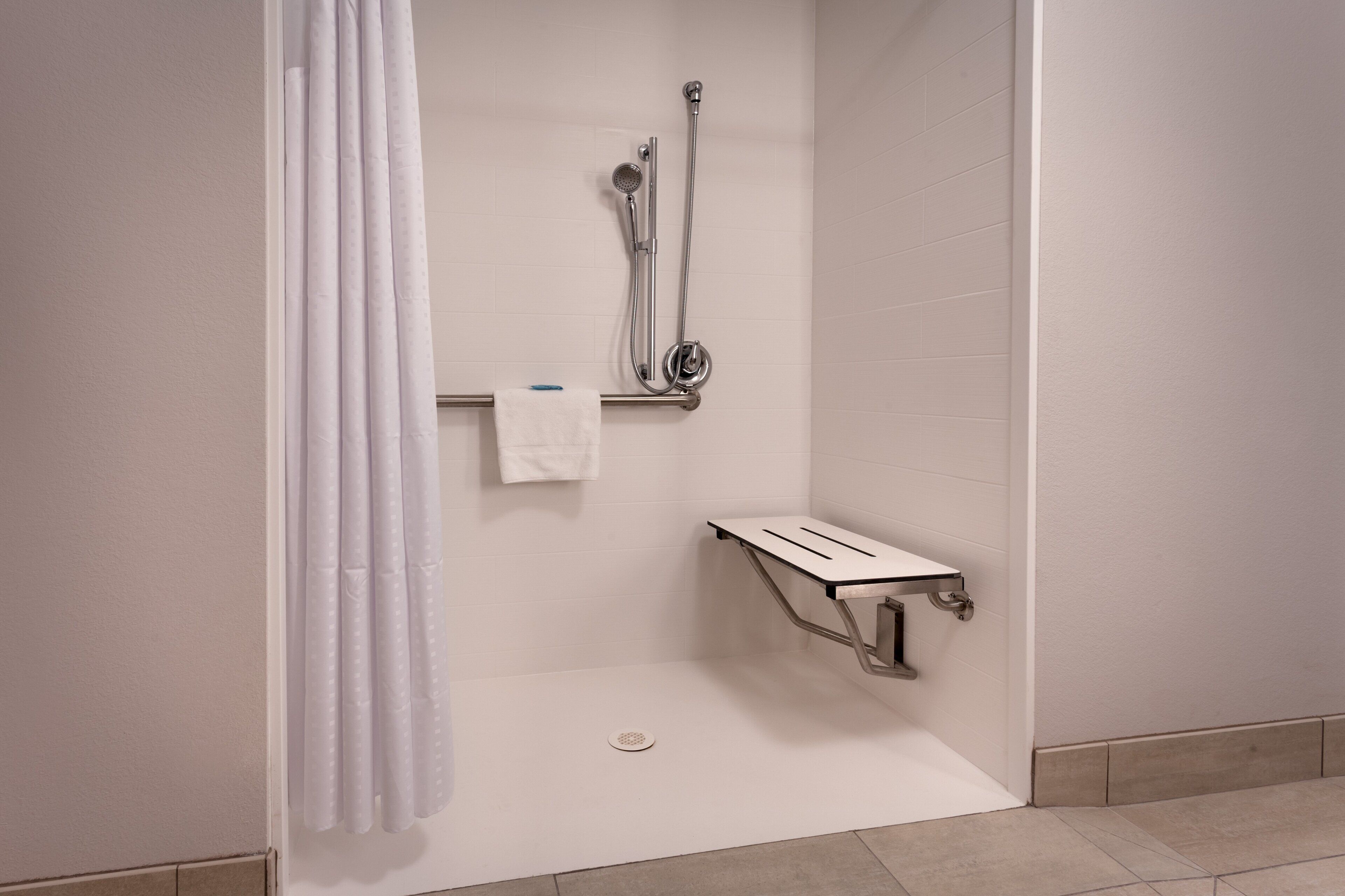 A shower area with a showerhead, a towel rack, and a small shelf.