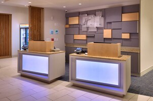 Zona de recepción de hotel con dos mostradores, un panel informativo en la pared y una máquina expendedora.