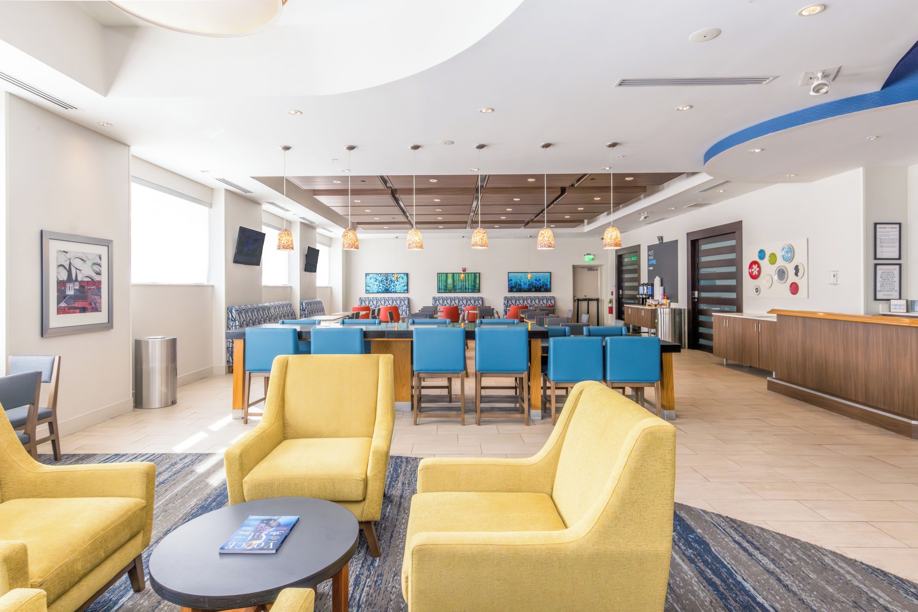 A hotel lobby with yellow armchairs, a coffee bar, and artwork on the walls.