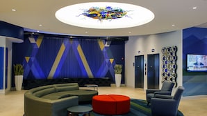 Eine moderne Lobby mit einer gebogenen Sitzecke, einem roten Hocker und einem Fernsehbildschirm.