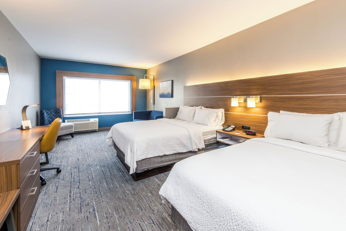 Ein Hotelzimmer mit zwei Betten, einem Schreibtisch, einem Stuhl, einem großen Fenster und einem an der Wand befestigten Telefon.