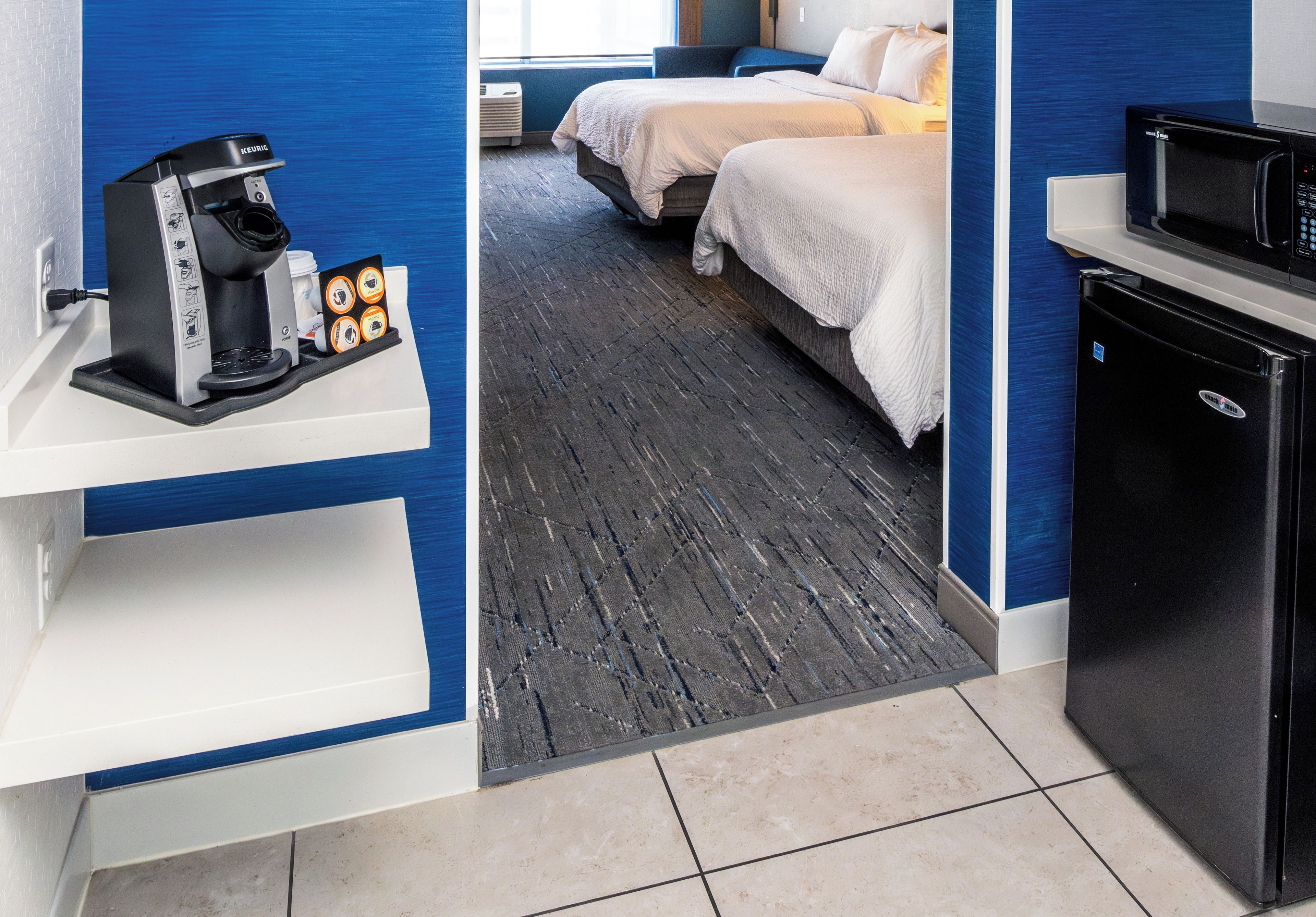 A hotel room with a coffee machine, a microwave, a bed, and a small refrigerator.
