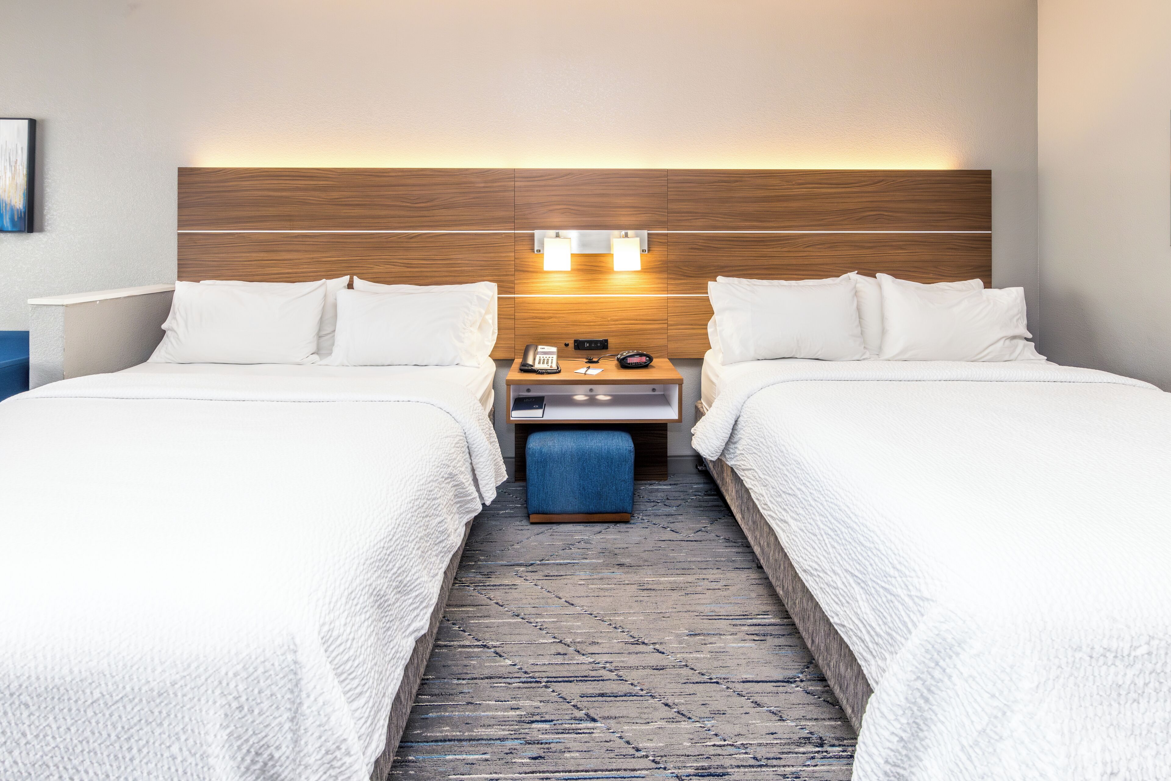 Une chambre d’hôtel avec deux lits, une table de chevet avec un téléphone et une horloge, et un luminaire fixé au mur.