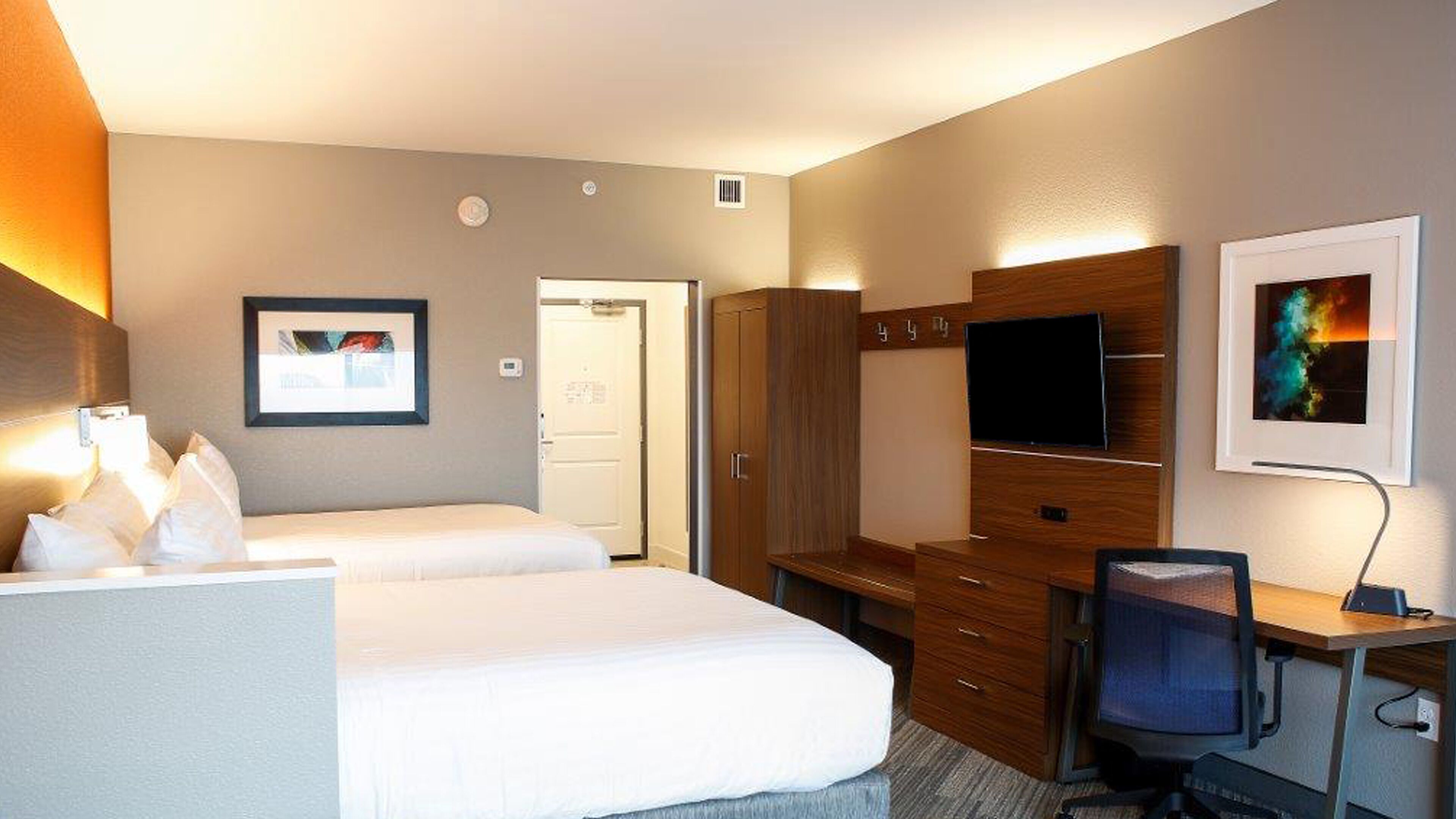 A hotel room with two beds, a desk with a chair, a television, and a wardrobe.