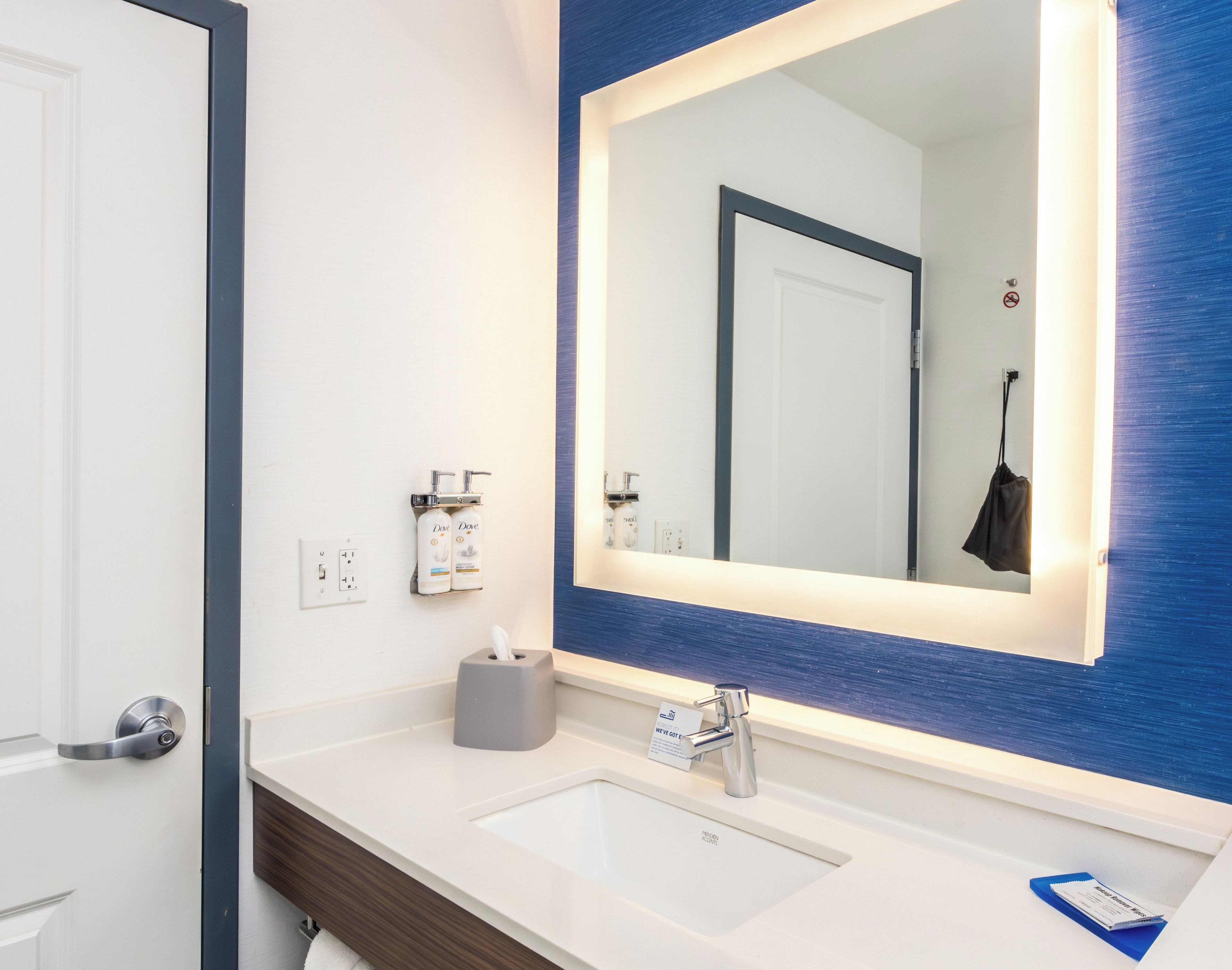 A bathroom with a white sink, a large mirror, and a blue accent wall.