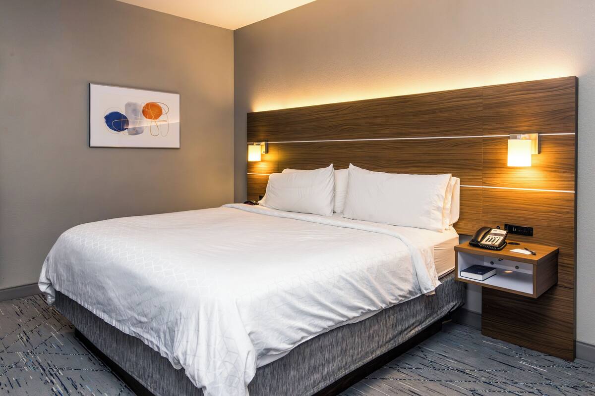 Ein Hotelzimmer mit einem großen Bett, einem Nachttisch mit Telefon und Buch sowie einer Wandleuchte.