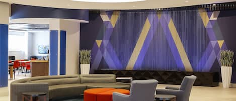 A modern lobby with a curved sofa, a round orange ottoman, and a seating area with chairs and a table.