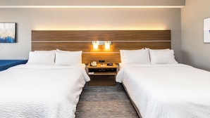 Ein Hotelzimmer mit zwei Betten, einem Holzkopfteil, Nachttischlampen, einem kleinen Tisch und einem gemusterten Teppich.