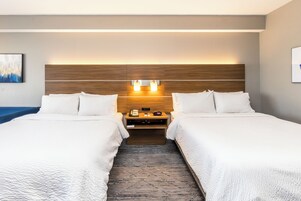Habitación de hotel con dos camas, cabecero de madera, lámparas de noche, una mesita y un tapete estampado.