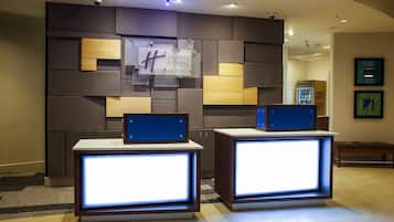 Un área de recepción de diseño moderno, con un letrero de Holiday Inn Express & Suites montado en la pared, un mostrador de recepción con paneles iluminados y un refrigerador al fondo.