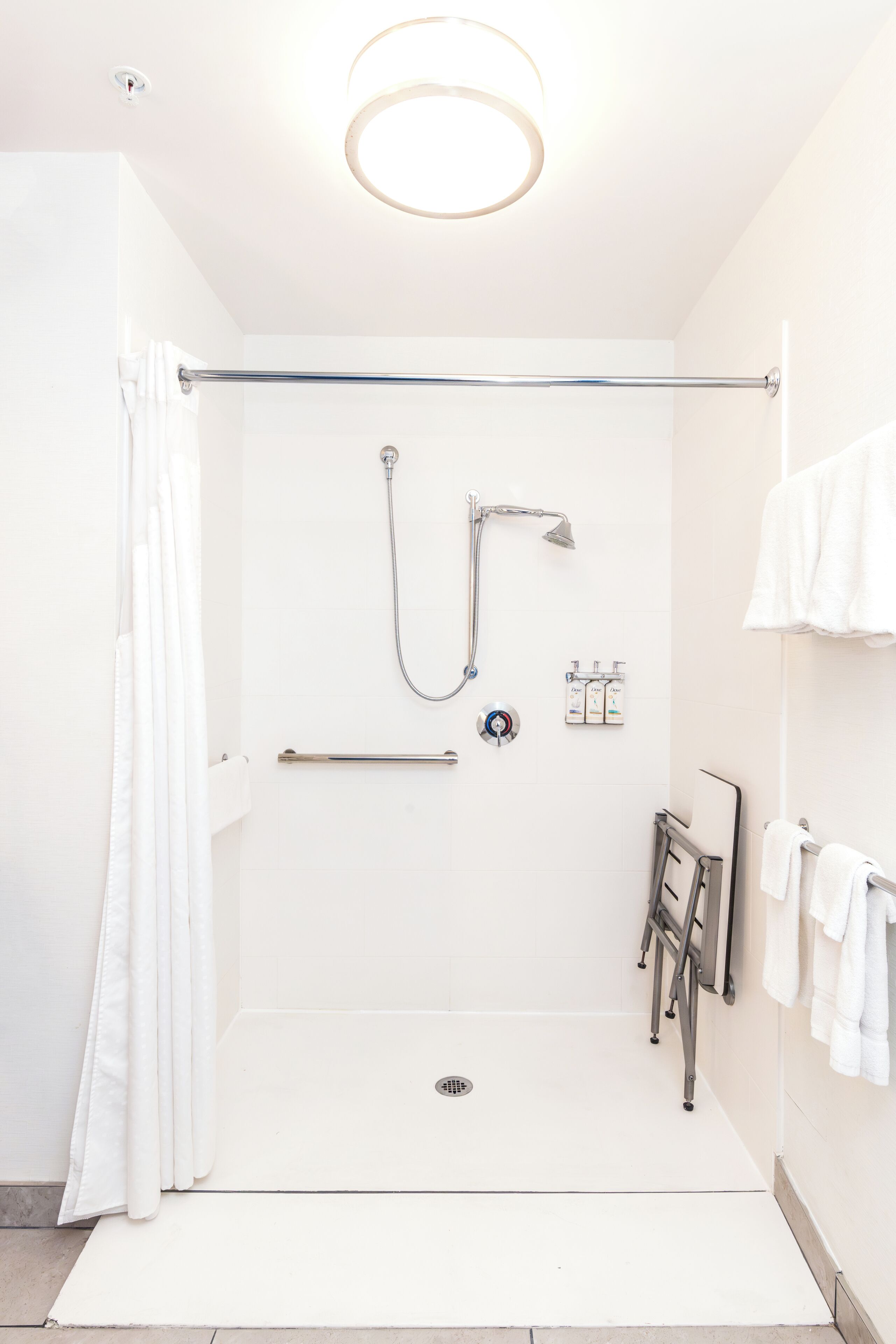 A modern bathroom with a walk-in shower, grab bars, a hand dryer, and a towel rack.
