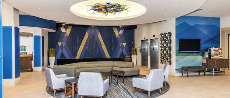 A modern lobby with a central seating area, a reception desk, and a large screen.