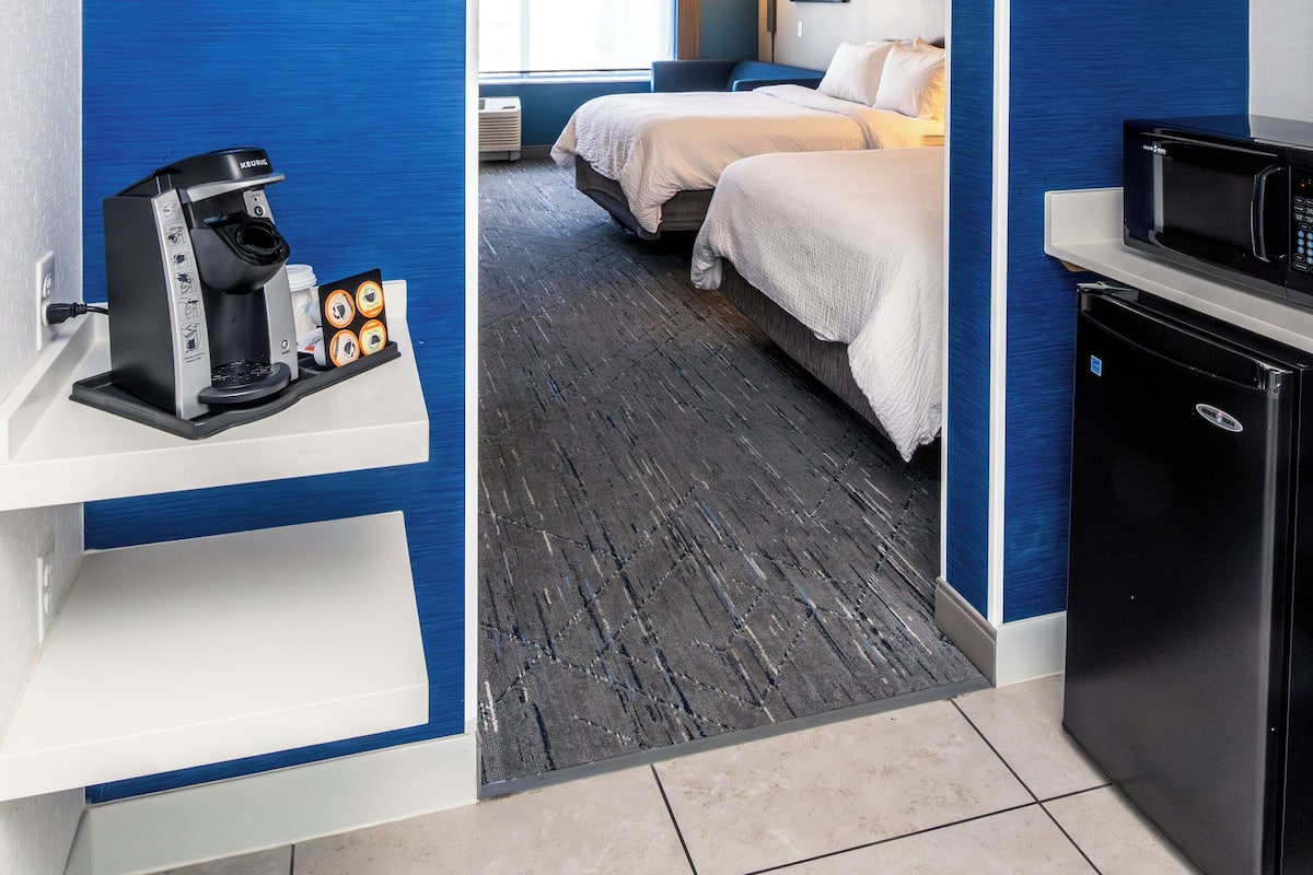 Ein Hotelzimmer mit blauer Akzentwand, einer Kaffeemaschine, einer Mikrowelle und einem Bett mit weißer Bettwäsche.