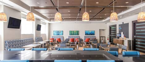 A modern dining area with blue and red seating, wooden tables, and decorative hanging lamps.