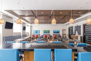 Un comedor moderno con asientos azules y rojos, mesas de madera y lámparas decorativas colgantes.