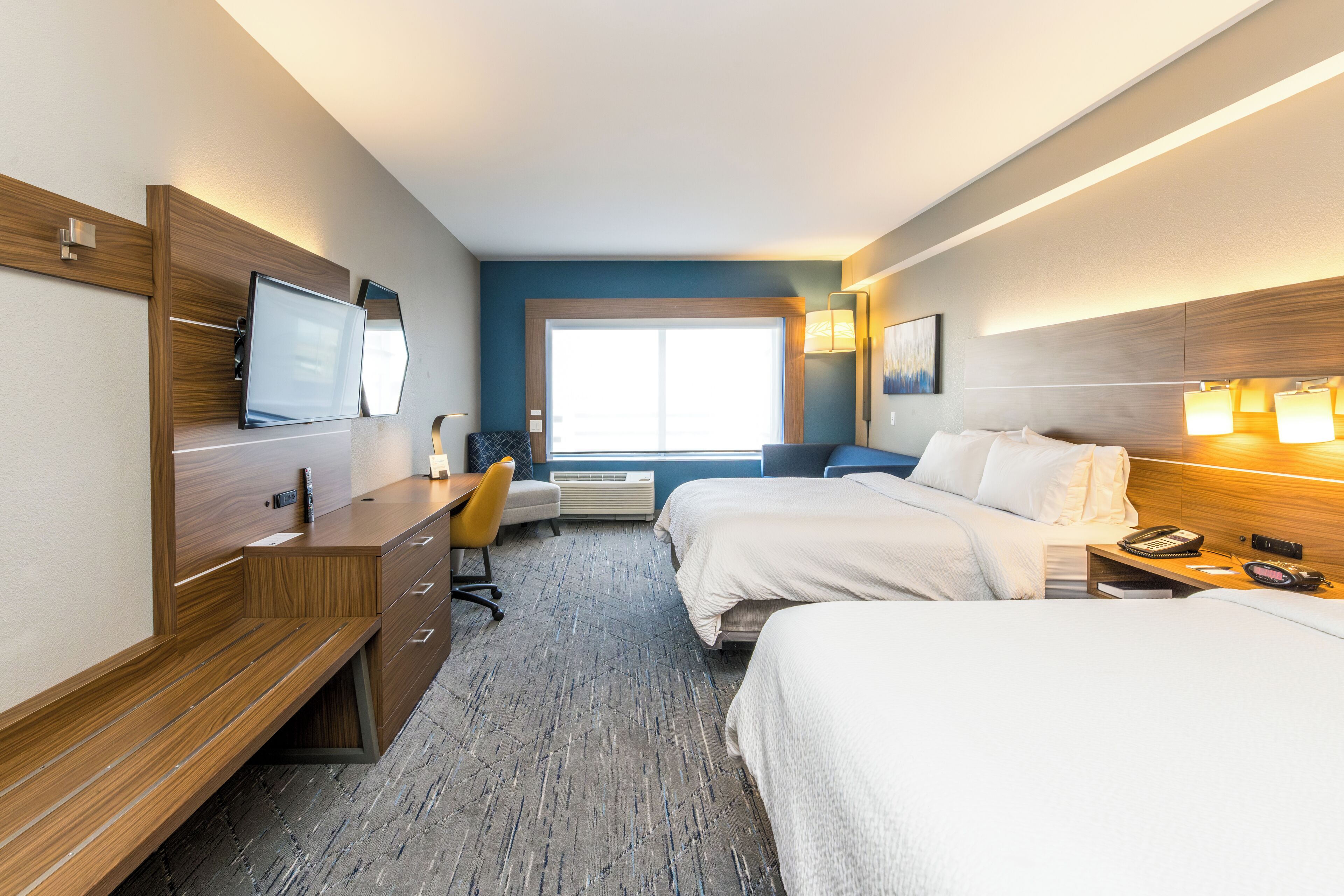 Habitación de hotel con dos camas, un escritorio, una silla, un televisor y una ventana.