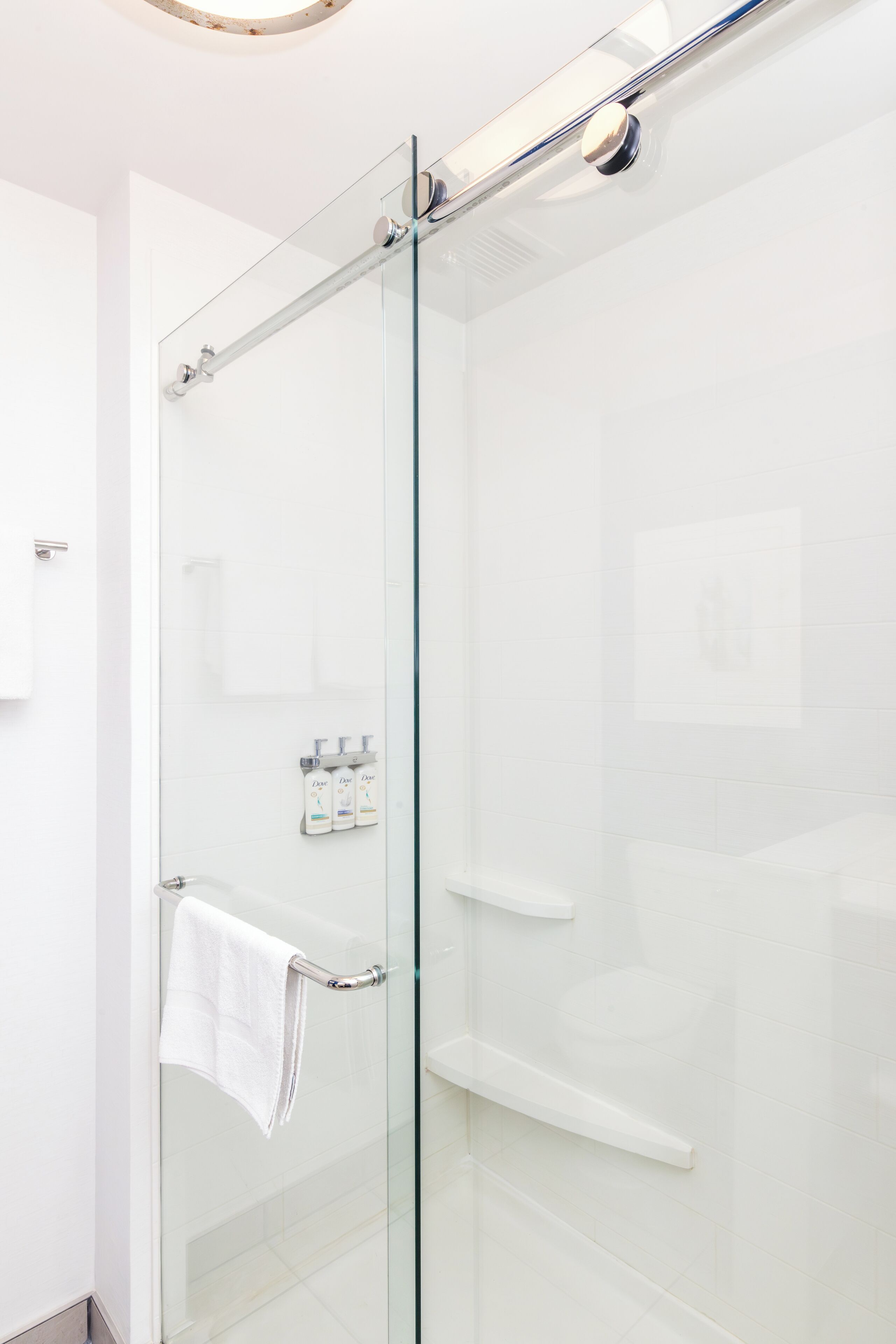 Une salle de bain moderne avec une douche à parois de verre, une serviette blanche suspendue à un porte-serviettes et une petite étagère contenant des articles de toilette.