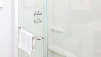 Un baño moderno con cabina de ducha de vidrio, una toalla blanca colgada en un perchero y un estante pequeño con artículos de aseo.