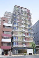 Un hotel de varios pisos con un llamativo letrero 'Grand Frisa', fachada de ladrillo y un diseño moderno con patrones de colores en las ventanas.