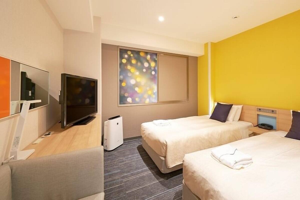 Een hotelkamer met twee bedden, een televisie, een raam met uitzicht en een muur met een kleurrijk abstract schilderij.