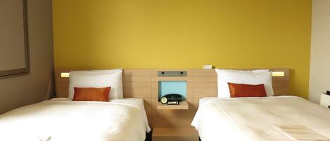 A hotel room with two beds, a wooden headboard, a bedside table with a phone, and a wall-mounted light.