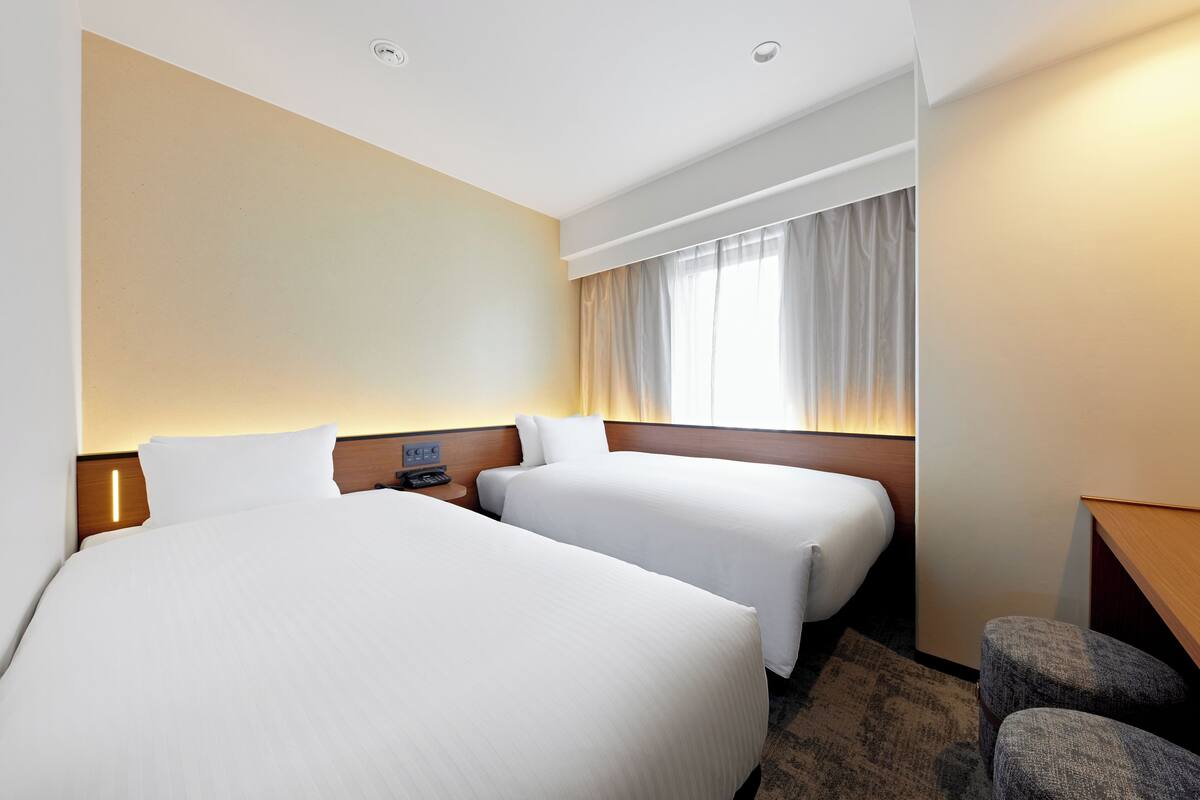 Een hotelkamer met twee bedden, een bureau, een stoel en een raam met gordijnen.