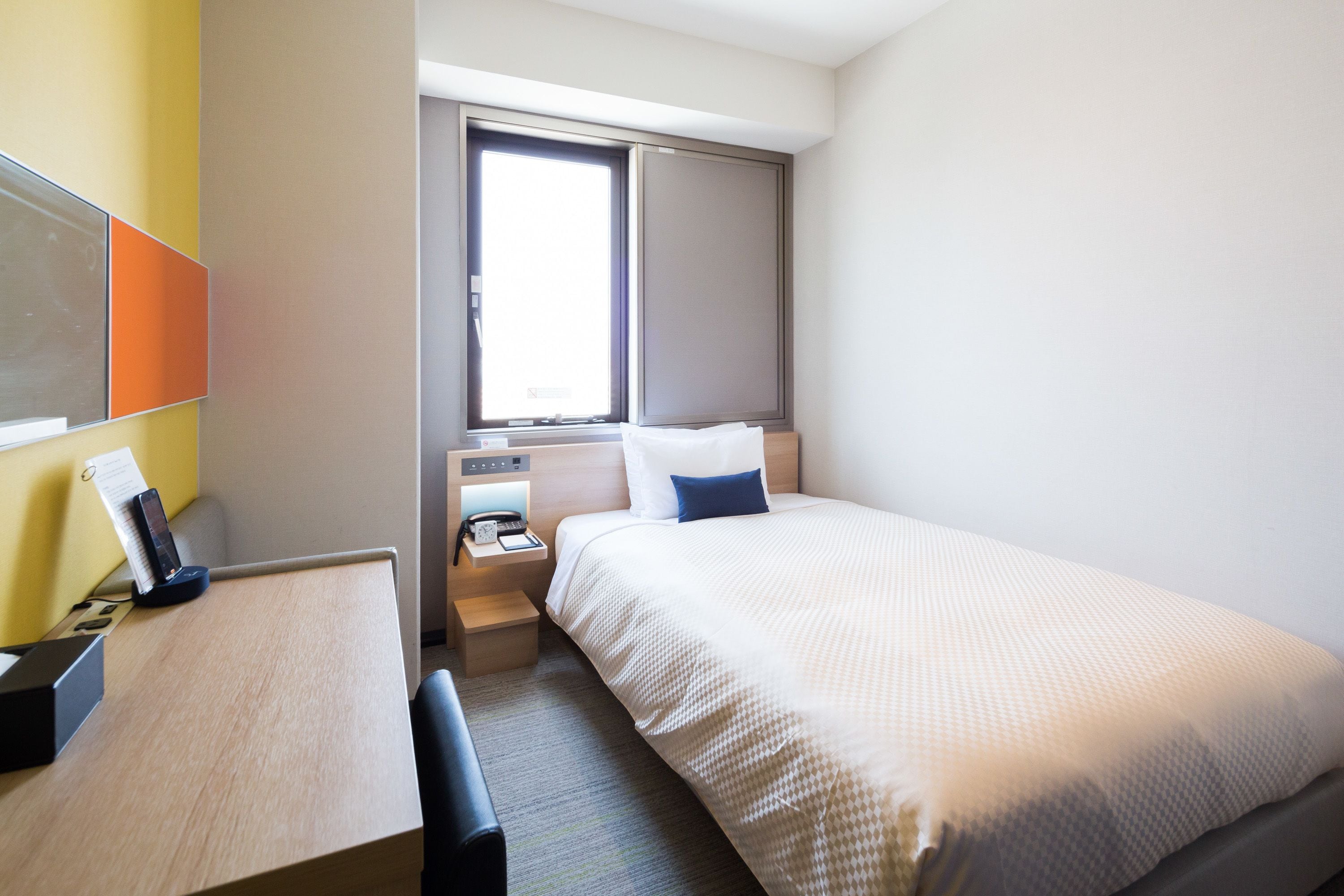 Una habitación de hotel con cama, mesita de noche y escritorio con teléfono y lámpara.