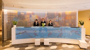 A reception desk with three staff members, a floral design on the counter, and a patterned floor. - Sotetsu Grand Fresa Osaka - Namba (Osaka)