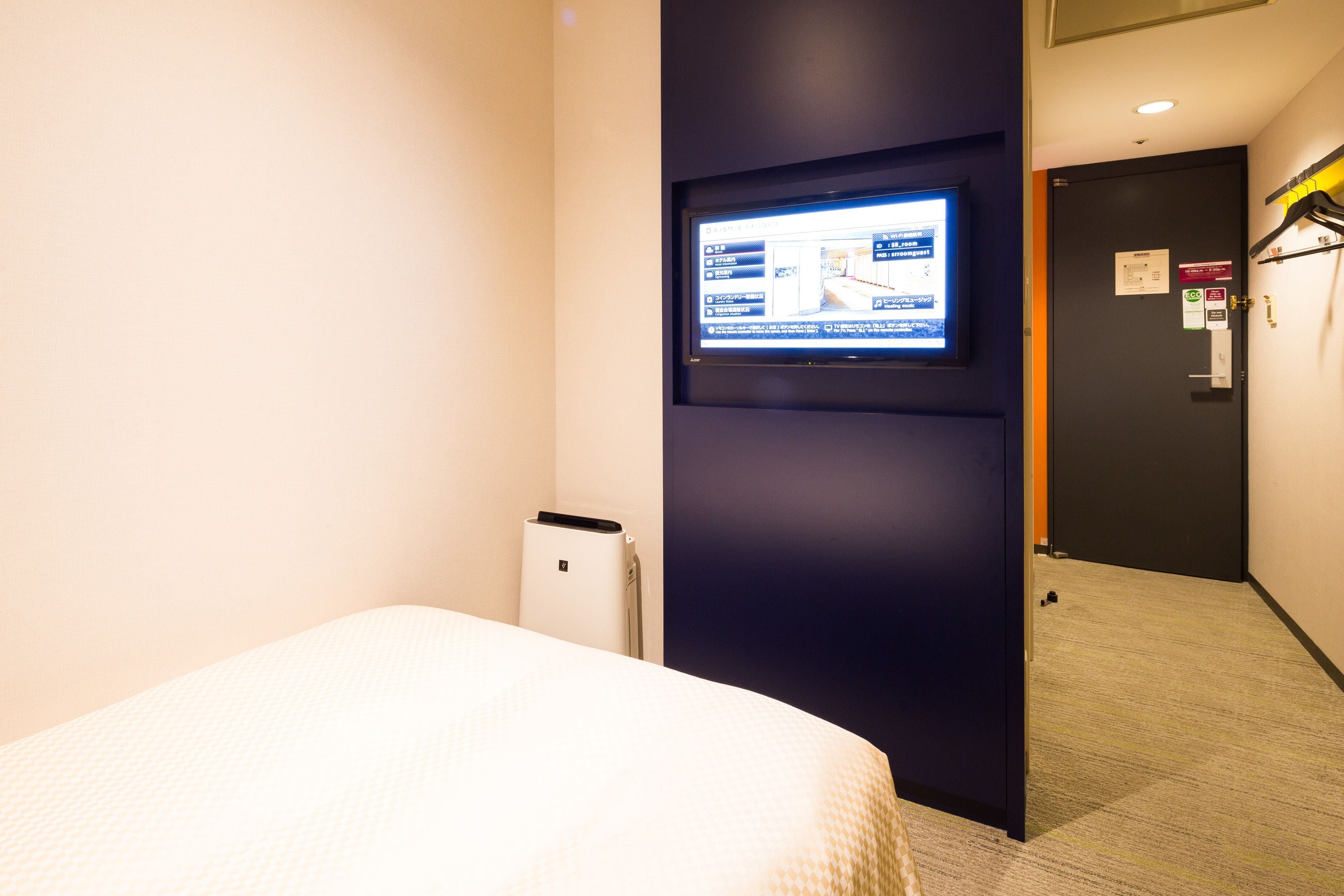 A hotel room with a bed, a television mounted on the wall, and a door with a coat rack.