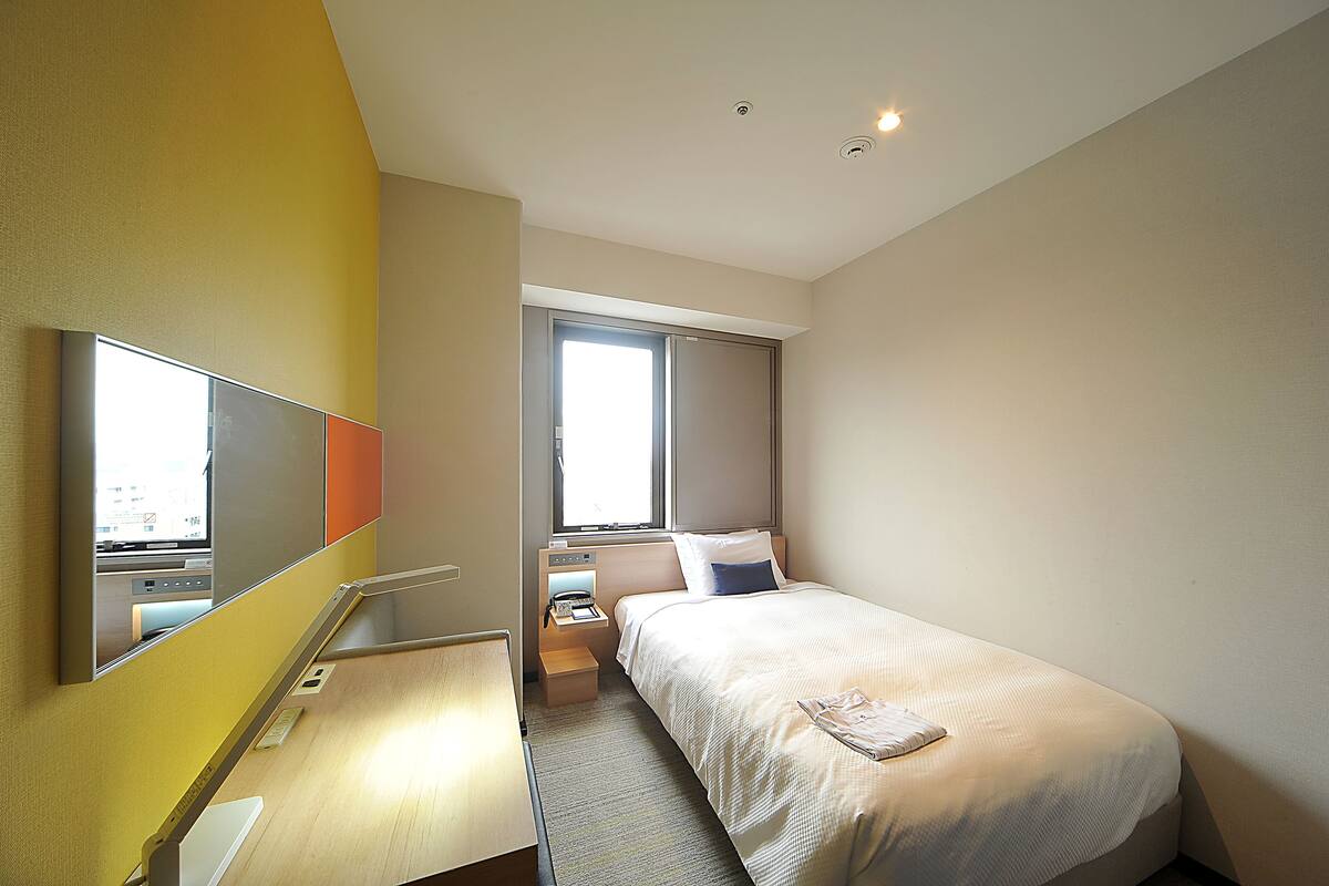Een hotelkamer met een bed, nachtkastje en een raam.
