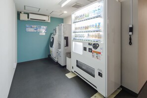 Een kamer met een automaat vol drankjes, een koelkast en een wasmachine.