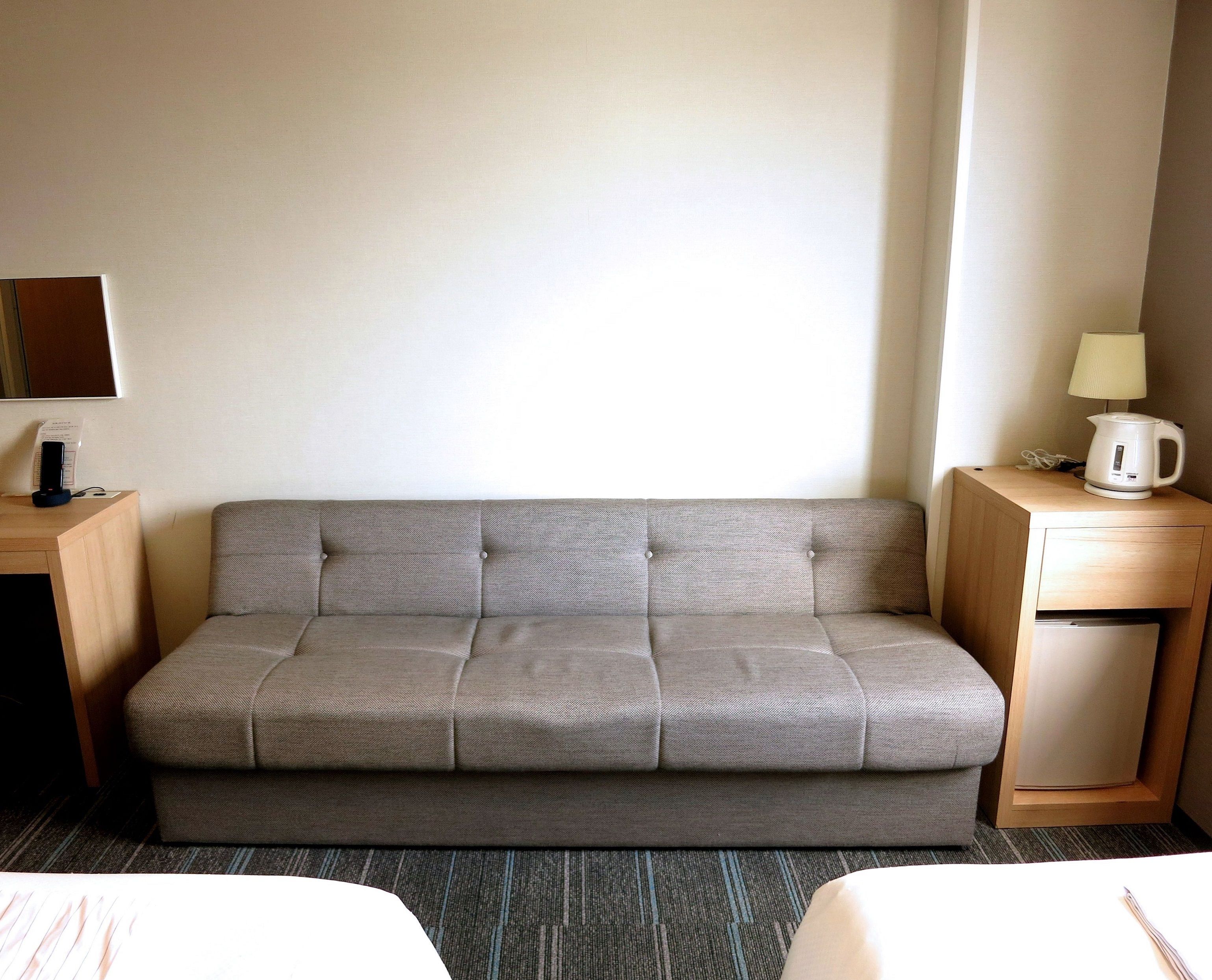 A neutral-colored sofa in a hotel room with a small table and a lamp on the right side.