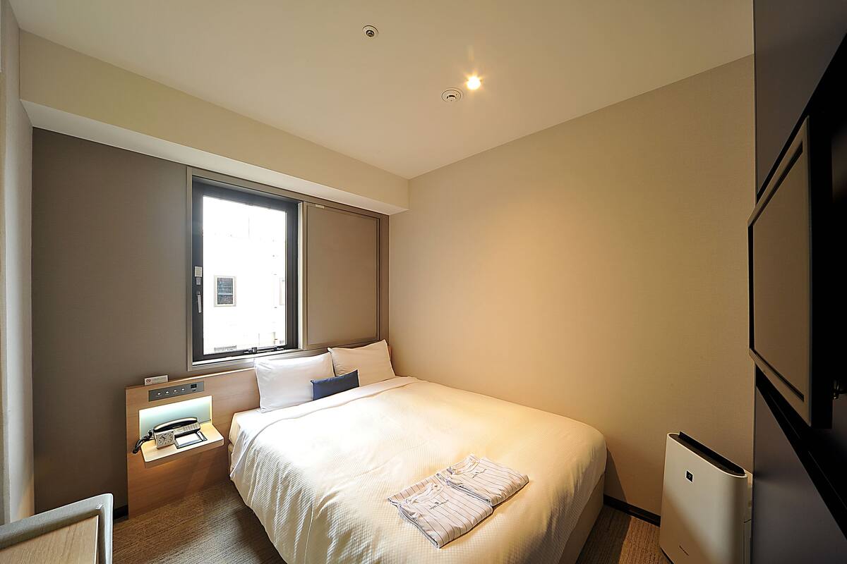 Een hotelkamer met een bed, nachtkastje en een raam.