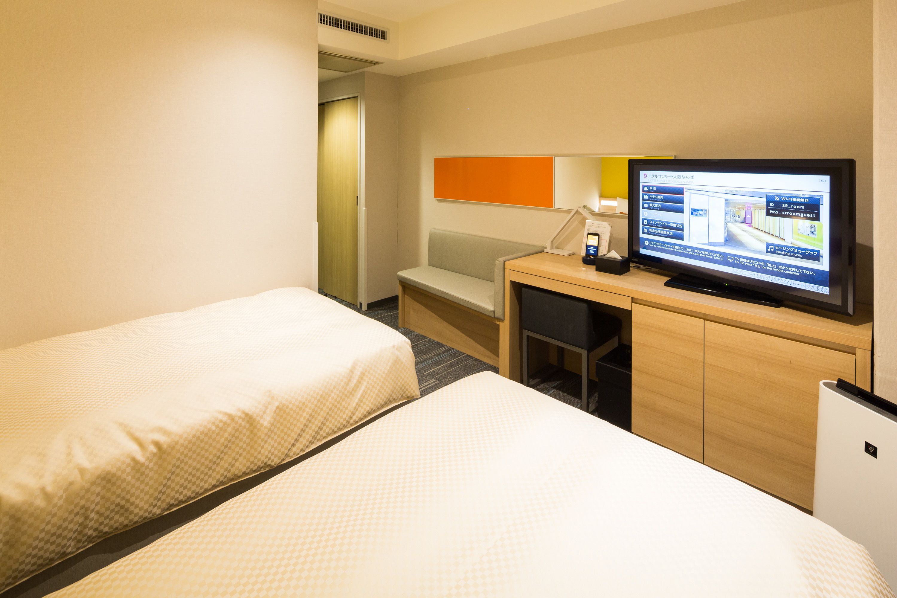 Ein Hotelzimmer mit zwei Betten, einem Schreibtisch mit Computer und einem Fernseher.
