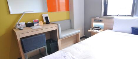 Habitación de hotel con cama, escritorio con silla, una mesita con teléfono, un cubo de basura y ventana con vista.